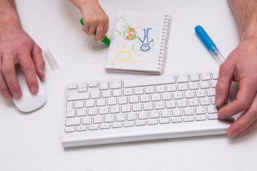Man's hands on a computer keyboard and mouse. Baby's hands with colourful markers and drawing. Man working at a computer with a child in his arms.  Working from home concept. 