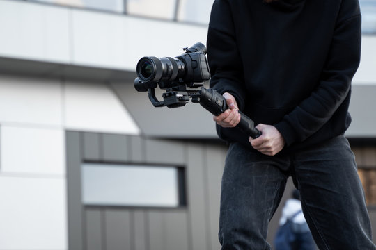 Professional videographer in black hoodie holding professional camera on 3-axis gimbal stabilizer. Filmmaker making a great video with a professional cinema camera. Cinematographer.
