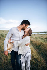 Happy couple in love hugging, kissing and smiling against the sky in field. Hat in girl's hand