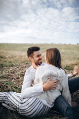 Lovely Сouple hugging, kissing and smiling against the sky seating on grass. Space for text