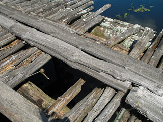 Naklejka premium Close-up of old wooden bridge over a small river in summer sunny day time. Blue sky and white clouds reflection on water