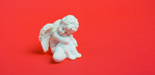 White angel figurine with heart on red background, Valentine's Day.