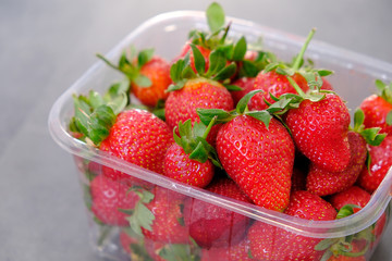 1 kg fresh strawberries in plastic box, on gray wooden background