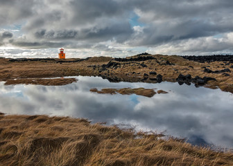 Orange Lighthouse with Clouds Reflecting in Pooled Water