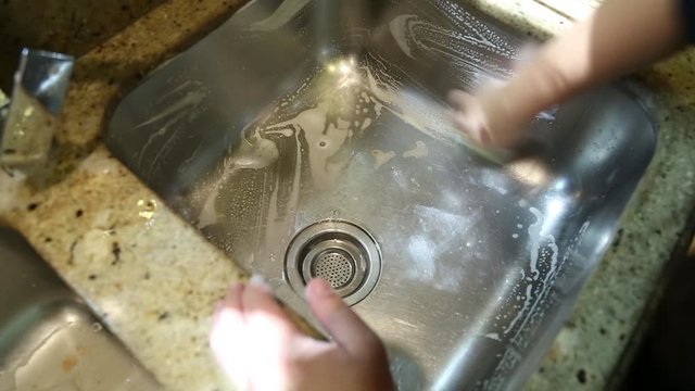 Washing a sink with sponge and rinse. Handheld shot. Close up