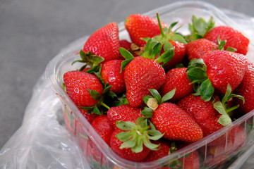 1 kg fresh strawberries in plastic box, on gray wooden background
