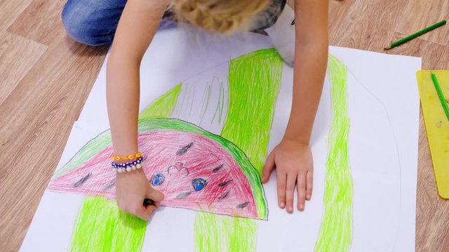 4k. Kids at home. Close up hands of little blonde girl drawing summer picture with watermelon on floor. Quarantine. Stay home.