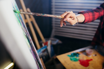 Close-up of the drawing a long with a brush on canvas watercolor abstract painting in green and purple colors.