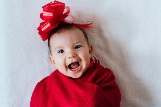 Portrait Of Happy Baby Girl With Red Ribbon On Her Head Wrapped In Red Blanket