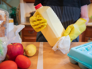 Coronavirus pandemic. Wiping food packages after shopping for groceries. Woman wearing gloves and using disinfectant sanitizing wipes to clean grocery items to prevent the spread of the COVID-19 virus