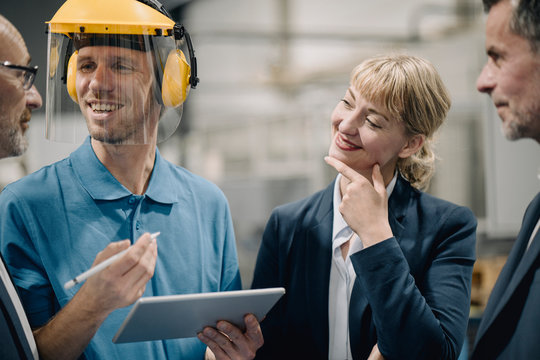 Business people and smiling worker with tablet talking in a factory