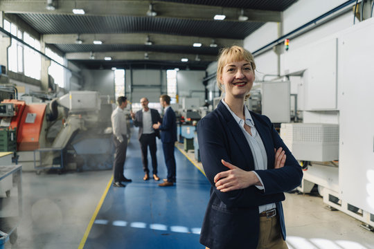 Portrait of a confident businesswoman in a factory with colleagues in backgound
