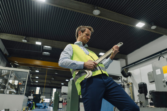 Man wearing reflective vest in a factory playing air guitar on large wrench