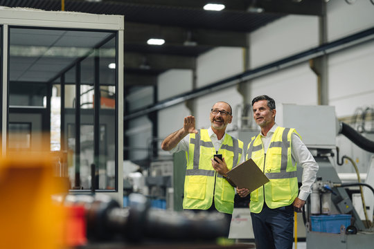 Two men in reflective vests talking in a factory