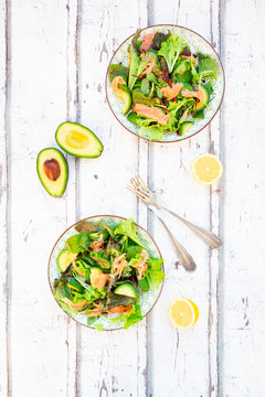 Two plates of ready-to-eat green salad with arugula, Lollo Rosso lettuce, baby spinach, beetroot leaves, avocado, corn salad and salmon