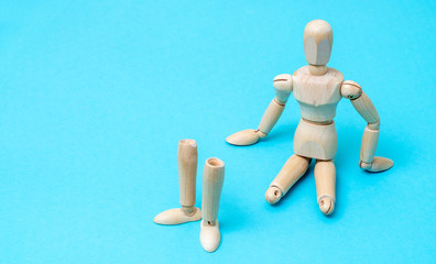 Wooden man mannequin sits without legs on a blue background. The concept of prostheses.