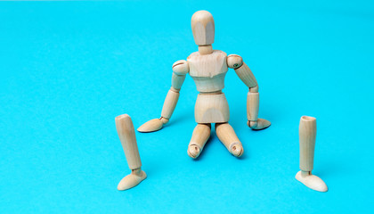 Wooden man mannequin sits without legs on a blue background. The concept of prostheses.