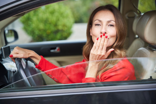 Portrait Of Smiling Mature Woman In Car Blowing A Kiss