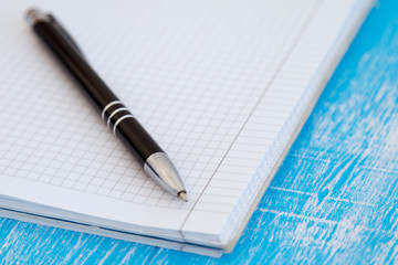 Close up pen and notebook for notes on a blue wooden background.