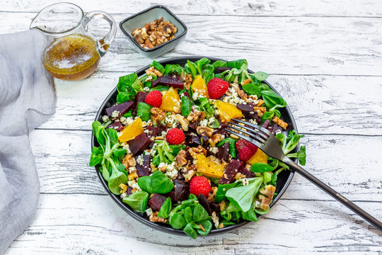 Plate of colorful mixed salad with feta cheese, common beet, walnuts, pine nuts, raspberries, oranges and corn salad