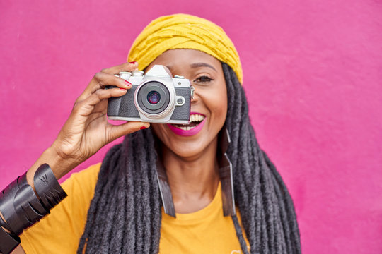 Portrait of woman with long dreadlocks and retro style camera in front of a pink wall