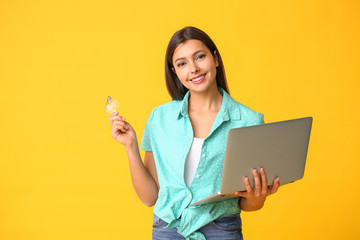 Young woman with laptop and credit card on color background. Online shopping concept