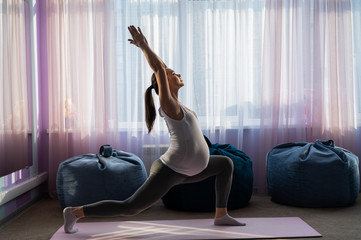 Pregnant woman practice yoga. A girl in the third trimester leads Pilates. Classes to prepare for childbirth. Waiting for the baby. Warrior Pose.