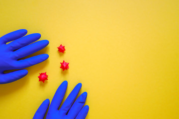 two rubber medical blue gloves on yellow background with small figures of coronavirus in between, copy space for your text