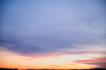 Landschaft mit Wolkengebilde und Mondsichel in Abenddämmernug