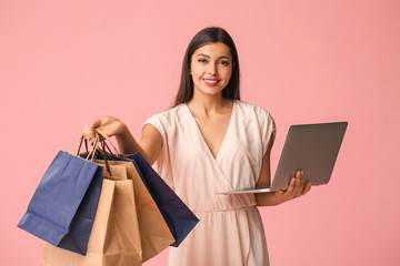 Young woman with laptop and shopping bags on color background