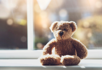 High key light sad teddy bear sitting near window in sunny day, Lonely brown bear sitting alone at home, Concept to social distancing , stay at home and prevent spread of virus and disease in Children