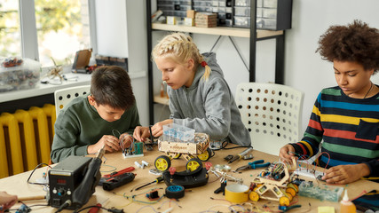 Giving solutions. Three kids building robots and vehicles at robotics lesson. Smart children and...