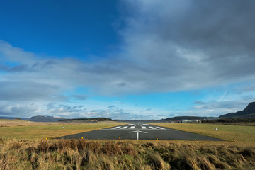 Small airport asphalt runway with markings for landings. Blue cloudy sky and fields around. Nobody.