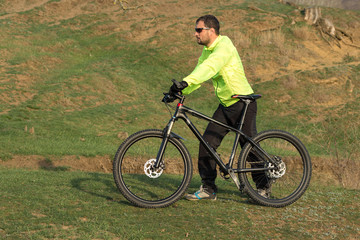 Obraz premium Cyclist in pants and green jacket on a modern carbon hardtail bike with an air suspension fork. The guy on the top of the hill rides a bike.