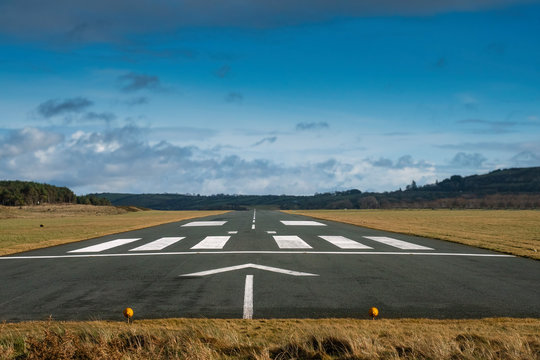 Small airport asphalt runway with markings for landings. Blue cloudy sky and fields around. Nobody.