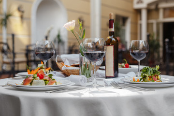 dinner table for four with a bottle of wine, salads, glasses on the street in the shadow of the yard
