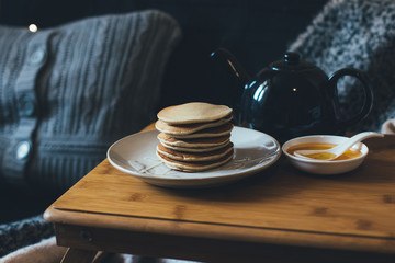 Pancakes with honey on wooden tray in cozy room.