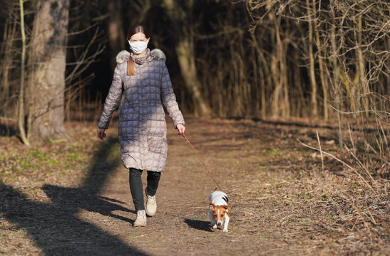 Young Woman In Warm Jacket, Wearing Virus Face Mouth Mask, Walks Her Dog On Country Road. Masks Are Mandatory   Outside Home During Coronavirus Covid-19 Outbreak In Some Countries