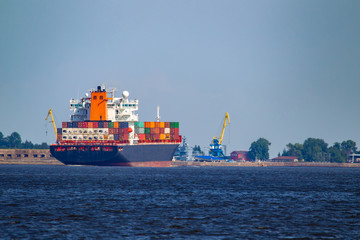 Fototapeta premium Cargo ships sailing off the coast. Container ship near the cargo port. Container ship on the background of blue sky. Shipping. Concept - Transfer of goods by water. Containers loaded on a sea vessel