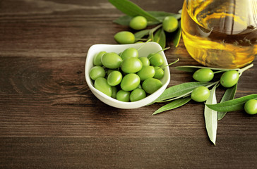 olive oil and fresh green olives on wooden background