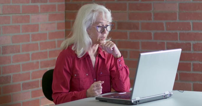 An older woman engaged in video chat with friends or family using the technology on her wireless laptop.