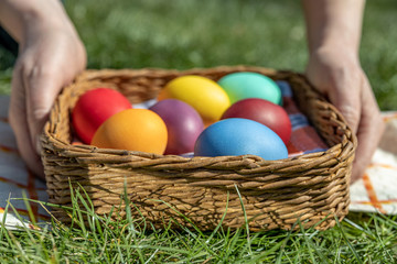 Female hands hold multi-colored Easter eggs in a basket on the grass, the background is blurred, shallow depth of field, selective focus. Easter holiday concept