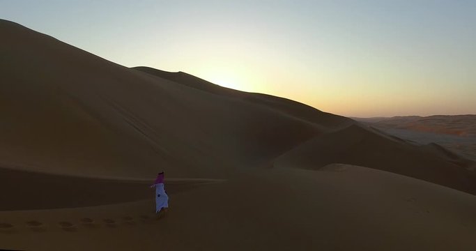 4K Drone Shot of Man Walking in Desert Sunset Over Sand Dunes in Dubai UAE Dressed in Traditional Clothes