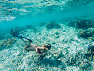 Young girl with diving mask and snorkel flippers in clear blue sea water, woman in red bikini swims in turquoise crystal transparent ocean water, tropical coral reef snorkeling on summer holidays