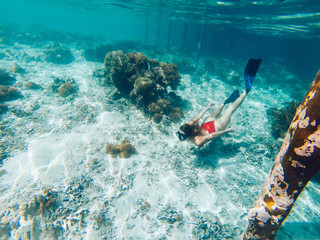Young girl with diving mask and snorkel flippers in clear blue sea water, woman in red bikini swims...