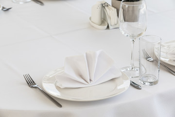 Serving a table in the restaurant waiting for guests and visitors. White tablecloth, napkins, plates and wine glasses. there is nobody