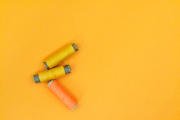 Yellow and orange spool of thread on a yellow background. The concept of needlework, sewing.