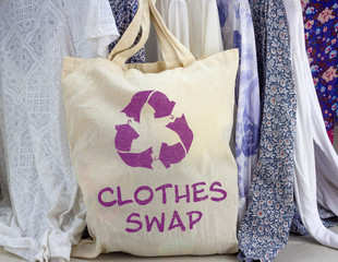 Clothes swap reusable bag with recycle textiles symbol in front of rack of clothes. Recycle clothes...