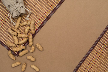 Nuts, shelled peanuts, sprinkle on the table from a linen bag, kraft paper background. Top view with copyspace, flat lay.