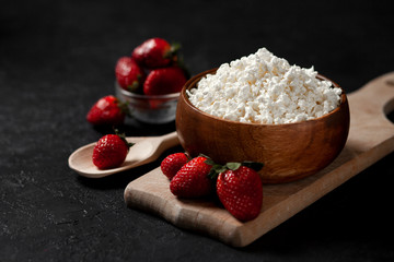 fresh homemade cottage cheese in a wooden plate with strawberries on a cutting board, healthy breakfast on a black table